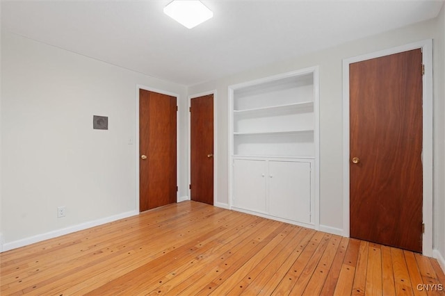 spare room featuring built in features, light wood-type flooring, and baseboards