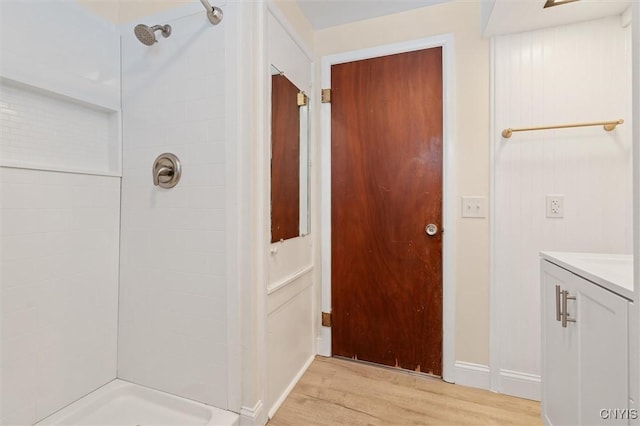 bathroom featuring baseboards, a tile shower, wood finished floors, and vanity