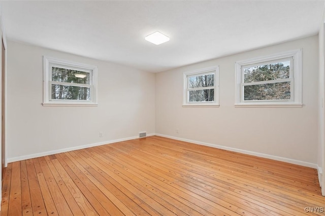 empty room with light wood-style floors, baseboards, visible vents, and a wealth of natural light