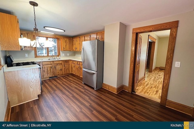 kitchen featuring range with gas cooktop, dark wood-style flooring, light countertops, hanging light fixtures, and freestanding refrigerator