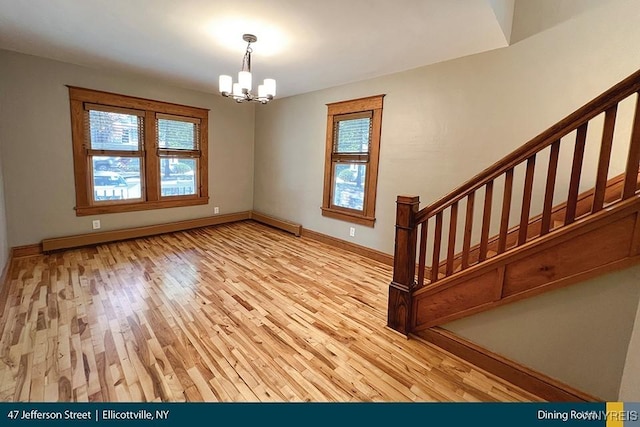 empty room featuring an inviting chandelier, a healthy amount of sunlight, light hardwood / wood-style floors, and baseboard heating