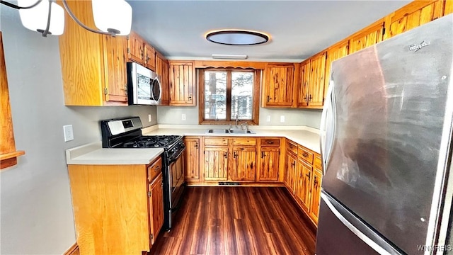 kitchen featuring appliances with stainless steel finishes, brown cabinets, dark wood-style flooring, light countertops, and a sink