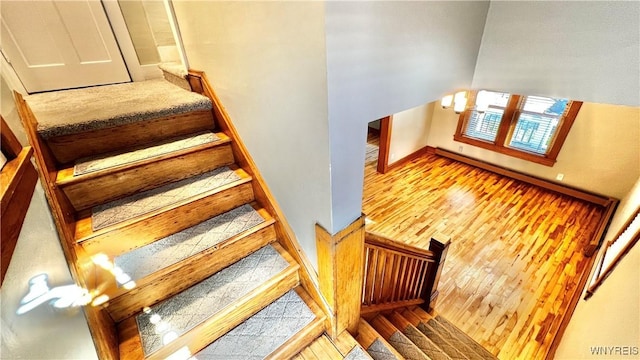 stairway featuring baseboards, a baseboard heating unit, and wood finished floors