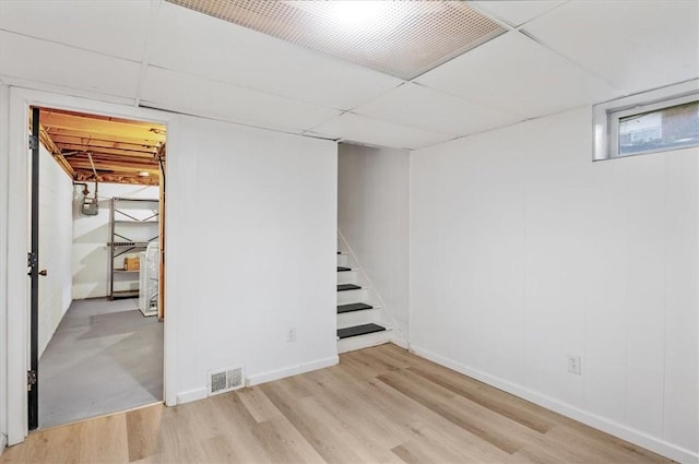 basement featuring a paneled ceiling and light hardwood / wood-style floors