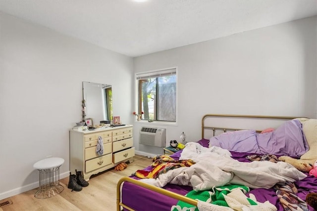 bedroom with a wall mounted air conditioner and light wood-type flooring