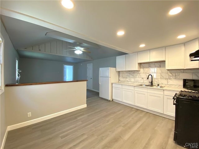 kitchen featuring sink, black gas stove, white cabinetry, white refrigerator, and vaulted ceiling