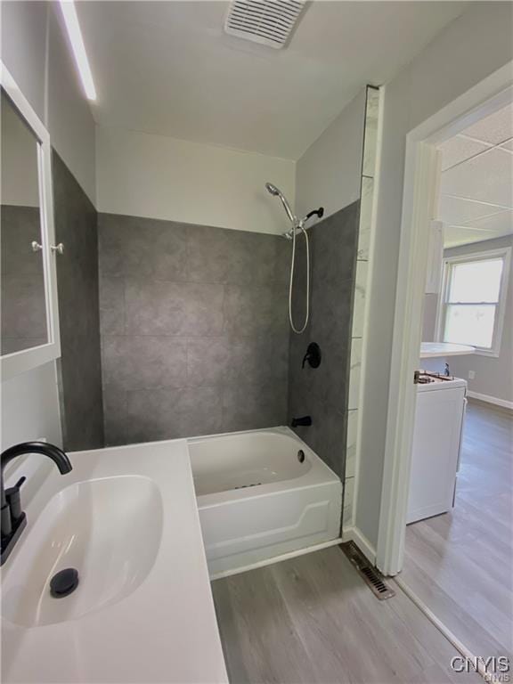 bathroom with wood-type flooring, tiled shower / bath combo, sink, and washer / dryer