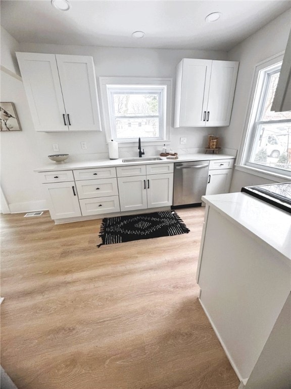 kitchen with white cabinetry, sink, stainless steel dishwasher, and light hardwood / wood-style floors