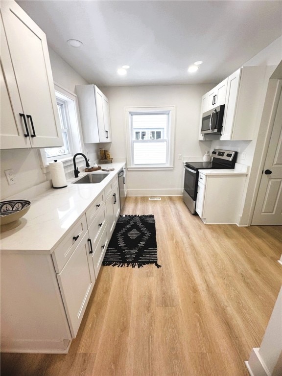 kitchen with sink, light hardwood / wood-style flooring, appliances with stainless steel finishes, plenty of natural light, and white cabinets