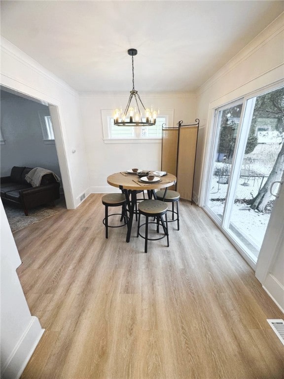 dining area featuring a notable chandelier, ornamental molding, light wood-type flooring, and a wealth of natural light