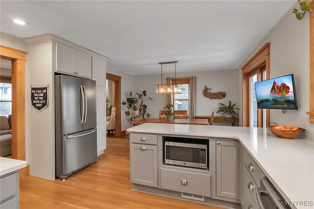 kitchen with gray cabinetry, an inviting chandelier, decorative light fixtures, light hardwood / wood-style flooring, and stainless steel appliances