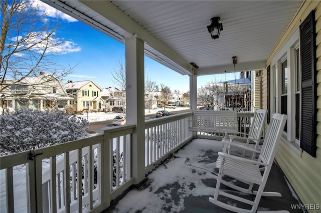 snow covered back of property featuring covered porch