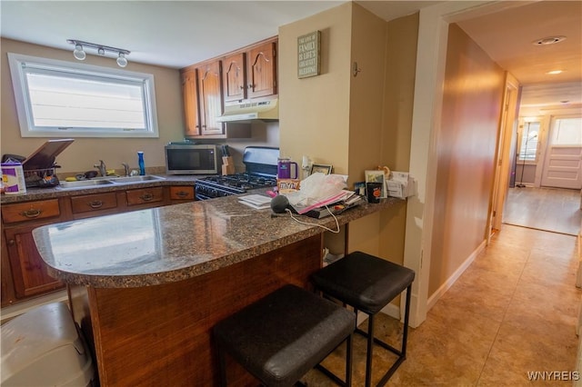 kitchen featuring sink, range with gas cooktop, kitchen peninsula, and a kitchen bar