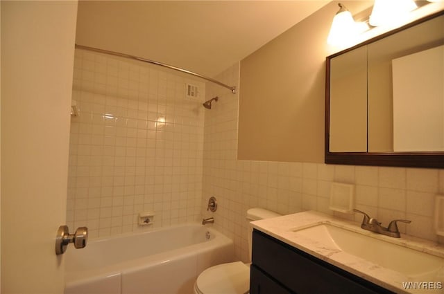 full bathroom featuring vanity, tiled shower / bath, toilet, and tile walls