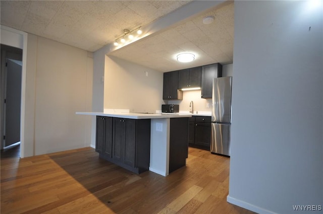 kitchen featuring stainless steel refrigerator, sink, a kitchen bar, light hardwood / wood-style floors, and kitchen peninsula