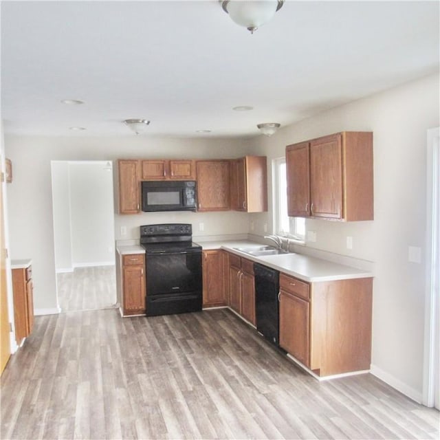 kitchen featuring light wood-style flooring, a sink, light countertops, black appliances, and brown cabinetry