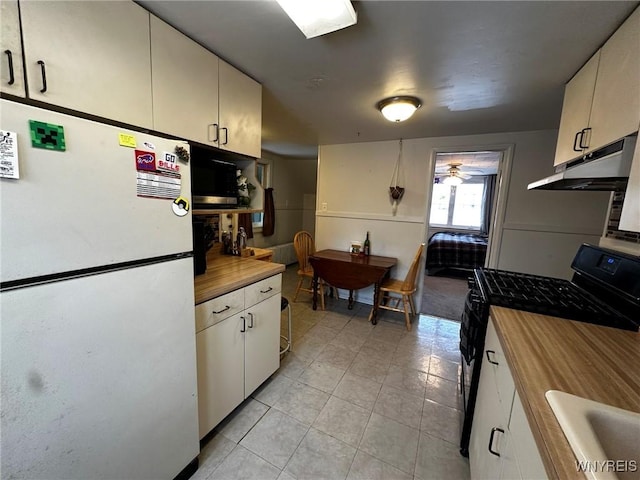 kitchen with sink, light tile patterned floors, black gas range, white cabinets, and white fridge