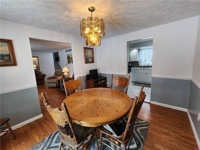 dining area with dark hardwood / wood-style floors, sink, a textured ceiling, and a notable chandelier