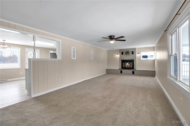 unfurnished living room with ornamental molding, ceiling fan with notable chandelier, and light colored carpet