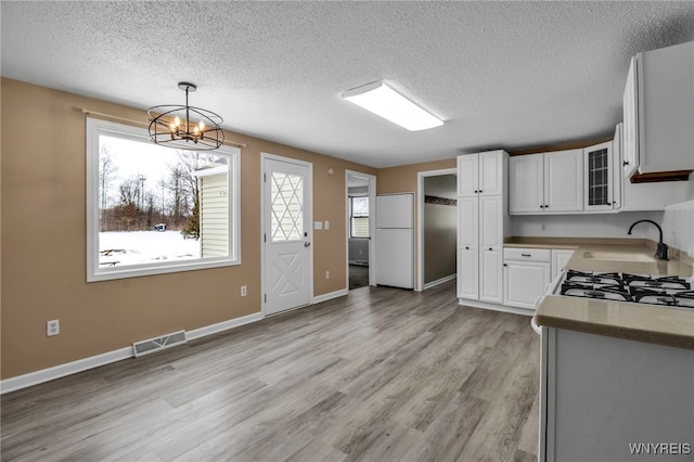 kitchen featuring sink, an inviting chandelier, hanging light fixtures, light wood-type flooring, and white cabinets