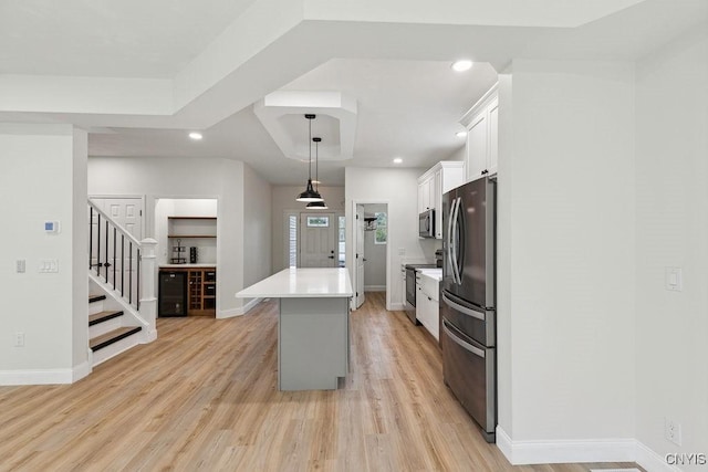 kitchen with appliances with stainless steel finishes, hanging light fixtures, a center island, white cabinets, and light wood-type flooring