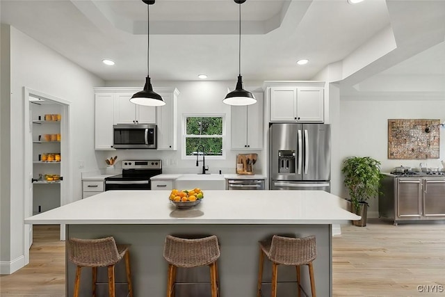 kitchen with sink, stainless steel appliances, a kitchen breakfast bar, a tray ceiling, and white cabinets