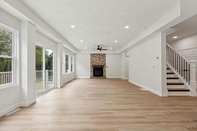 unfurnished living room featuring light hardwood / wood-style flooring, a fireplace, a raised ceiling, and ceiling fan