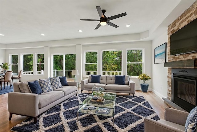 living room featuring a stone fireplace, ceiling fan, and light wood-type flooring