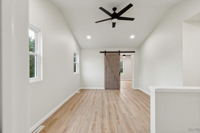 empty room with light hardwood / wood-style flooring, a barn door, ceiling fan, and vaulted ceiling