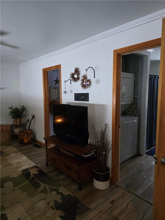 living room featuring dark wood-type flooring, ornamental molding, and stacked washer and clothes dryer