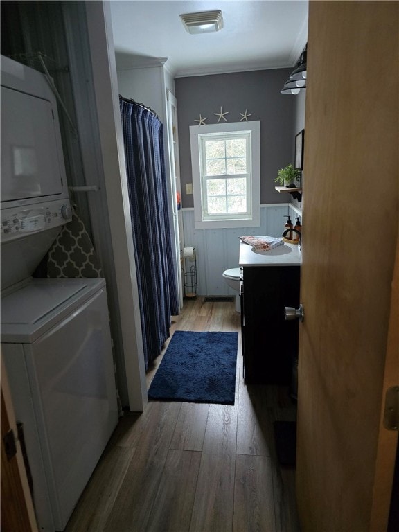 bathroom featuring stacked washing maching and dryer, wood-type flooring, vanity, toilet, and crown molding