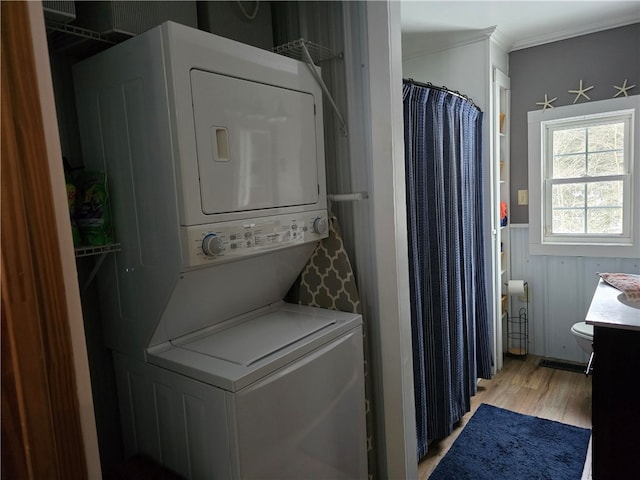 laundry room with crown molding, stacked washer / drying machine, and light hardwood / wood-style floors