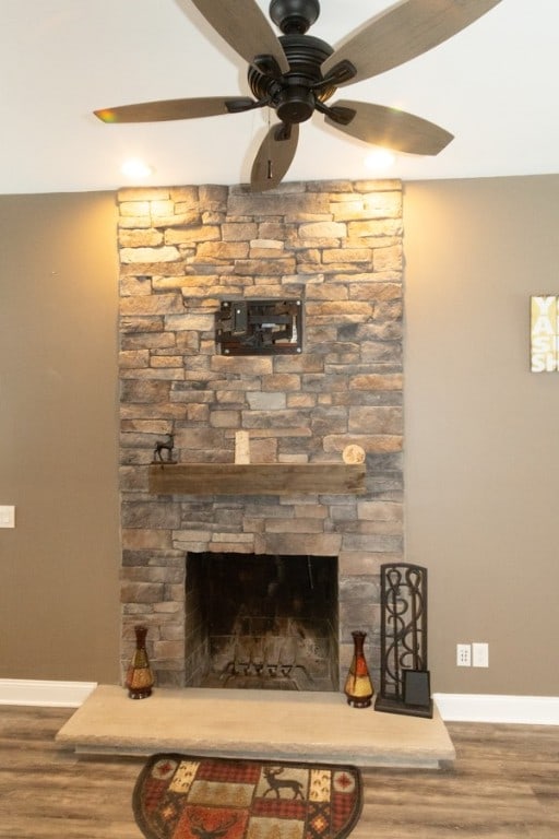 room details with a stone fireplace, wood-type flooring, and ceiling fan