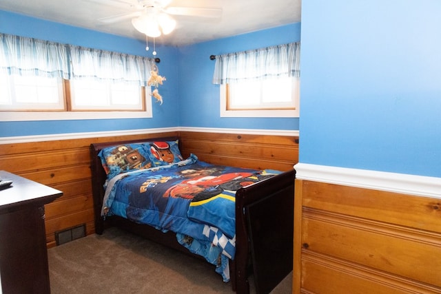 carpeted bedroom featuring multiple windows, ceiling fan, and wooden walls