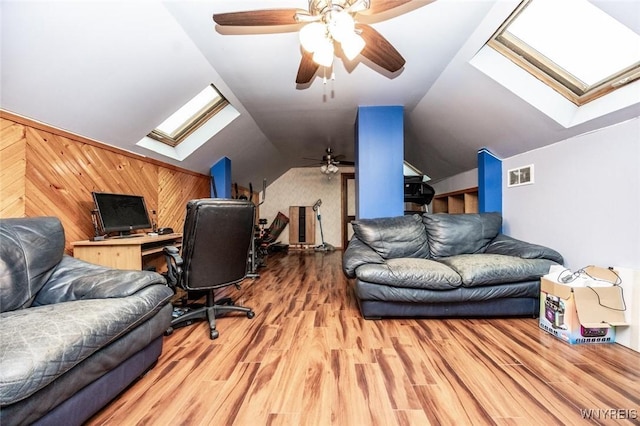 office space featuring ceiling fan, light hardwood / wood-style flooring, vaulted ceiling with skylight, and wood walls