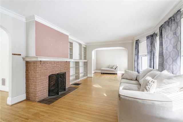 living room with hardwood / wood-style flooring, ornamental molding, built in shelves, and a brick fireplace