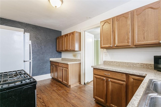 kitchen with white refrigerator, dark hardwood / wood-style flooring, range with gas stovetop, and sink