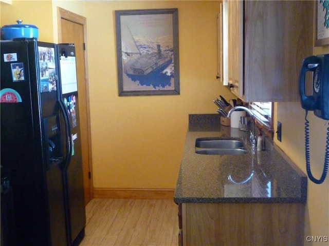 kitchen with sink, dark stone countertops, light hardwood / wood-style floors, and black refrigerator with ice dispenser