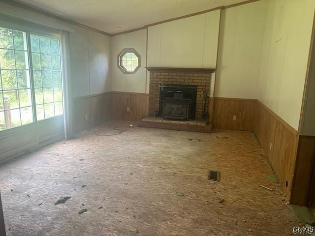 unfurnished living room featuring crown molding, wooden walls, and a fireplace