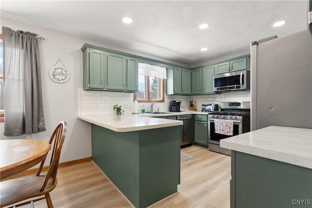 kitchen featuring stainless steel appliances, kitchen peninsula, green cabinetry, and light wood-type flooring