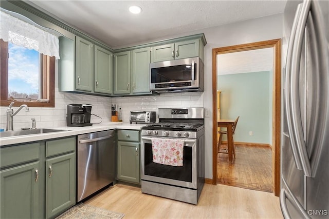 kitchen featuring sink, green cabinets, backsplash, stainless steel appliances, and light hardwood / wood-style floors