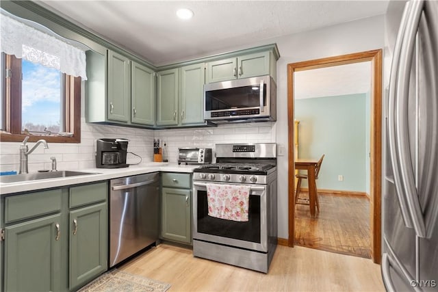 kitchen with green cabinetry, appliances with stainless steel finishes, sink, and light wood-type flooring