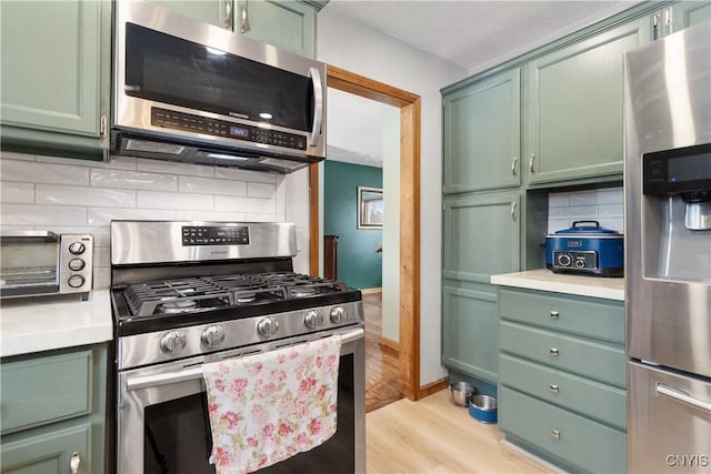 kitchen with stainless steel appliances, green cabinets, and backsplash