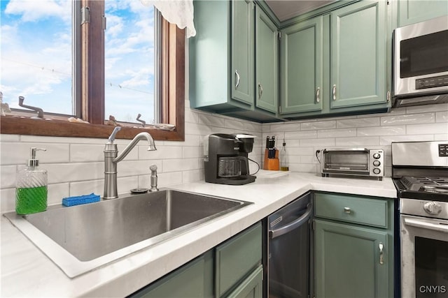 kitchen featuring stainless steel appliances, sink, backsplash, and green cabinetry