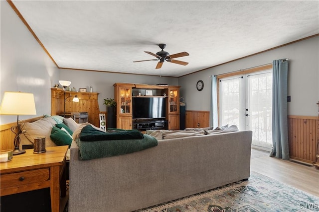 living room featuring french doors, wood walls, light hardwood / wood-style flooring, ornamental molding, and ceiling fan