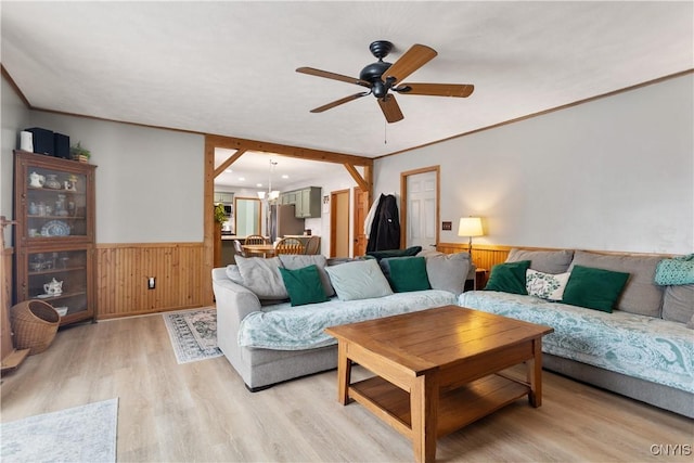 living room featuring ornamental molding, ceiling fan with notable chandelier, light hardwood / wood-style floors, and wood walls