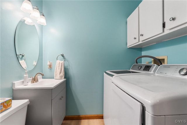 washroom with sink, light hardwood / wood-style flooring, washing machine and dryer, and cabinets