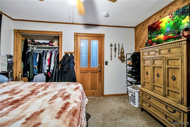 carpeted bedroom featuring wooden walls, ornamental molding, a closet, and ceiling fan