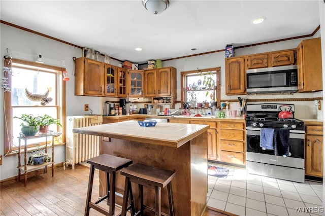 kitchen featuring a kitchen bar, crown molding, appliances with stainless steel finishes, radiator heating unit, and a kitchen island