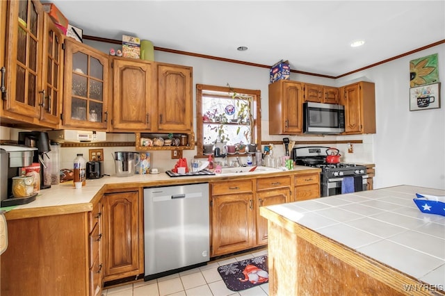 kitchen featuring sink, tile counters, stainless steel appliances, and ornamental molding